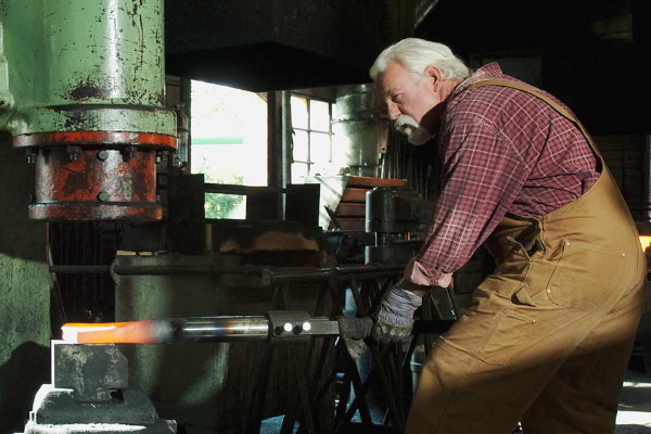 A man shaping a molten billet with a hydraulic press in a workshop