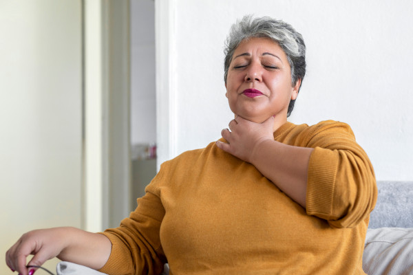 A woman holds her throat as she deals with heartburn/acid reflux