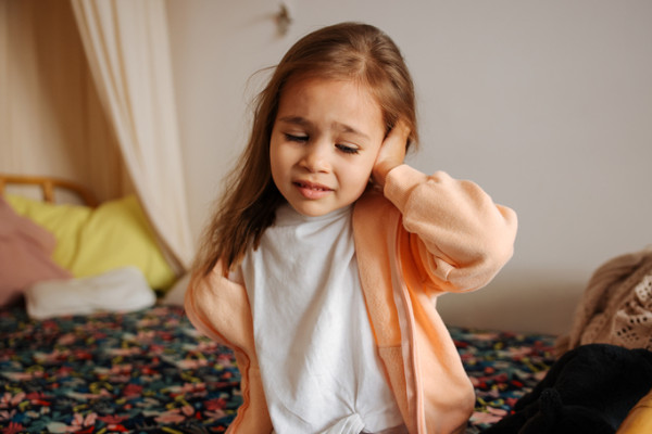 A child holding their hand to their ear as if irritated