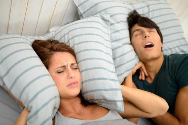 A woman covering her ears with her pillow while her partner's snoring keeps her awake