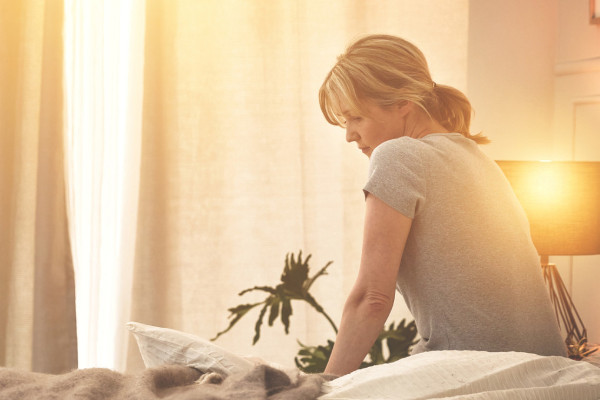 A woman sits on the side of her bed contemplating her restless night's sleep