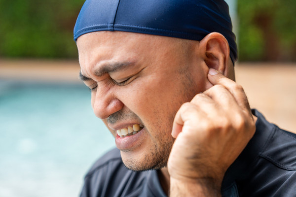 A man wearing a swim cap rubbing his ear in discomfort