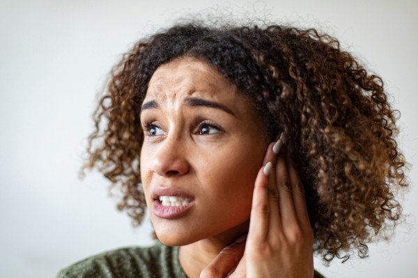 A woman holding her ear and grimacing in pain due to tinnitus