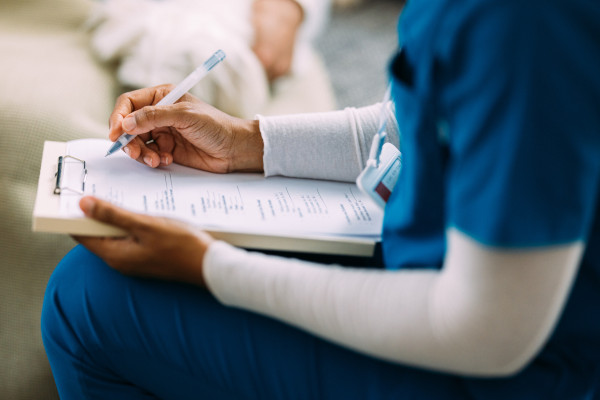 A nurse is writing on a clipboard during a patient consultation, representing healthcare communication, professionalism, and patient care.