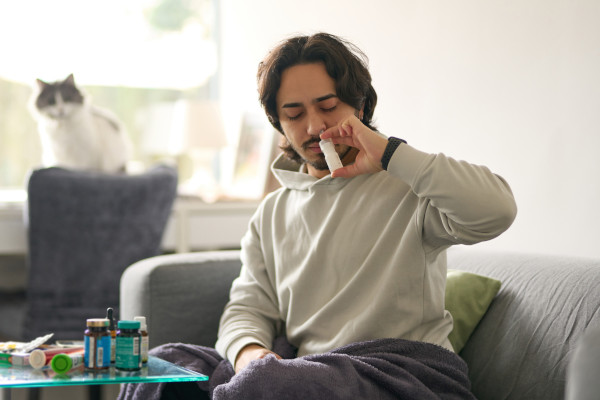 A man using nasal spray while sitting on his couch
