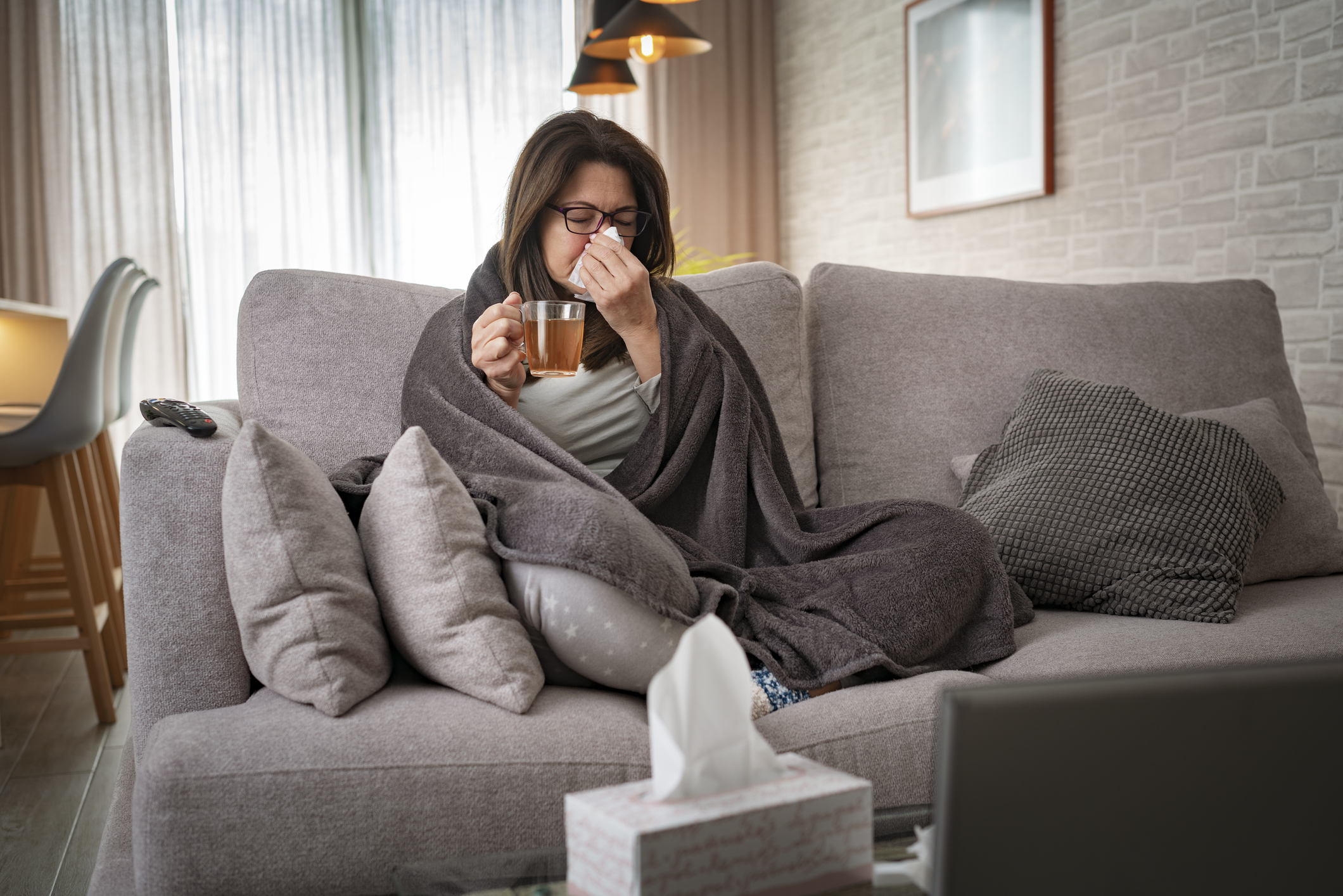 A woman sitting on her couch surrounded with blankets and tissues, suffering from chronic rhinitus